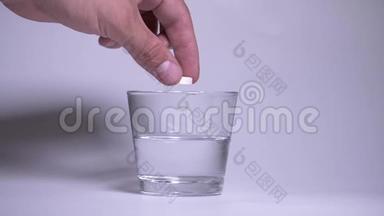 男人的手把橙色的泡腾片扔进一杯水里。 水中的气泡、水沸腾和喷射都会使药丸溶解